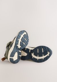 Sportiniai batai su tekstūruotu alyvuogių žalios spalvos viršumi, mėlynos gumos padu ir baltais akcentais. Juose yra paminkštintas apykaklė ir pyni batraiščiai.