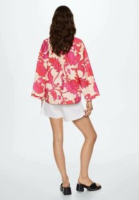 Top oversize a fantasia floreale nei toni del rosa e corallo con maniche a campana. Indossato sopra pantaloni corti bianchi e sandali con piattaforma neri.
