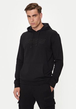 Felpa nera con tasca a marsupio e cappuccio con cordino. Presenta il logo "GUESS" in rilievo sul davanti. Taglio dritto e materiale morbido.