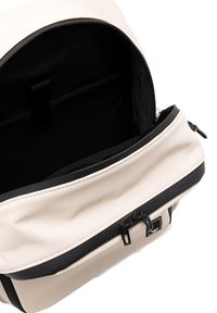 Zaino crema e nero con una texture liscia, scomparto principale con zip, tasche interne e dettagli neri. Include un'etichetta con logo.