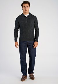 Ciemnoszary sweter z dzianiny warkoczowej z kołnierzem i guzikami, w połączeniu z niebieskimi dżinsami i brązowymi wiązanymi butami. Gładka faktura dzianiny, casualowy design.