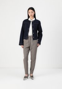 En denimjacka i mörkblått med knappstängning, bärs över en vit skjorta med krage. Grå skräddarsydda byxor och metalliska skor fulländar outfiten.