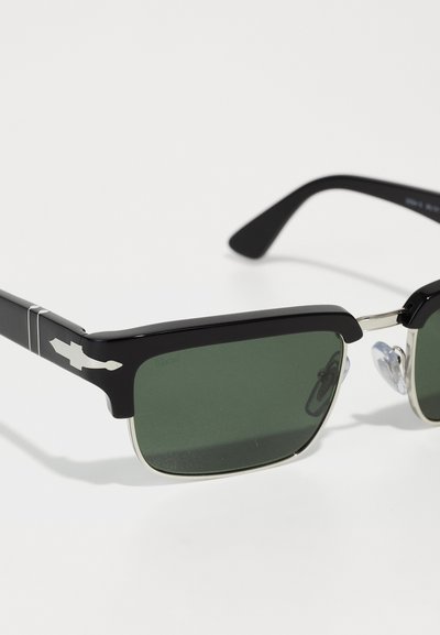 Ochelari de soare negri cu lentile de culoare verde, de formă rectangulară, cu accente din metal și un logo distinctiv pe rama templului.