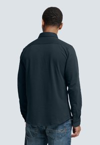 Diepblauwe langemouwen overhemd met een kraag, rechte snit en knopenmanchetten, gecombineerd met denim jeans in een relaxte pasvorm. Eenvoudige ontwerpelementen zichtbaar.