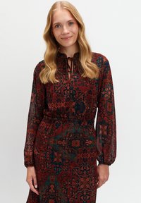 Długo-sleeve burgundowa sukienka w wzór paisley w odcieniach niebieskiego, zielonego i pomarańczowego. Posiada zawiązywany dekolt oraz elastyczny pas, co zapewnia dopasowany krój.