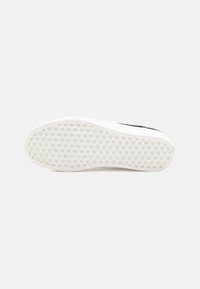 Black sneaker with a textured white rubber sole featuring a diamond pattern. The design includes a smooth, matte finish on the upper.