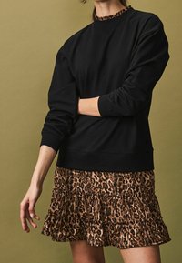 Sweat-shirt noir avec un col rond et des poignets côtelés, associé à une jupe à volants arborant un motif léopard marron.