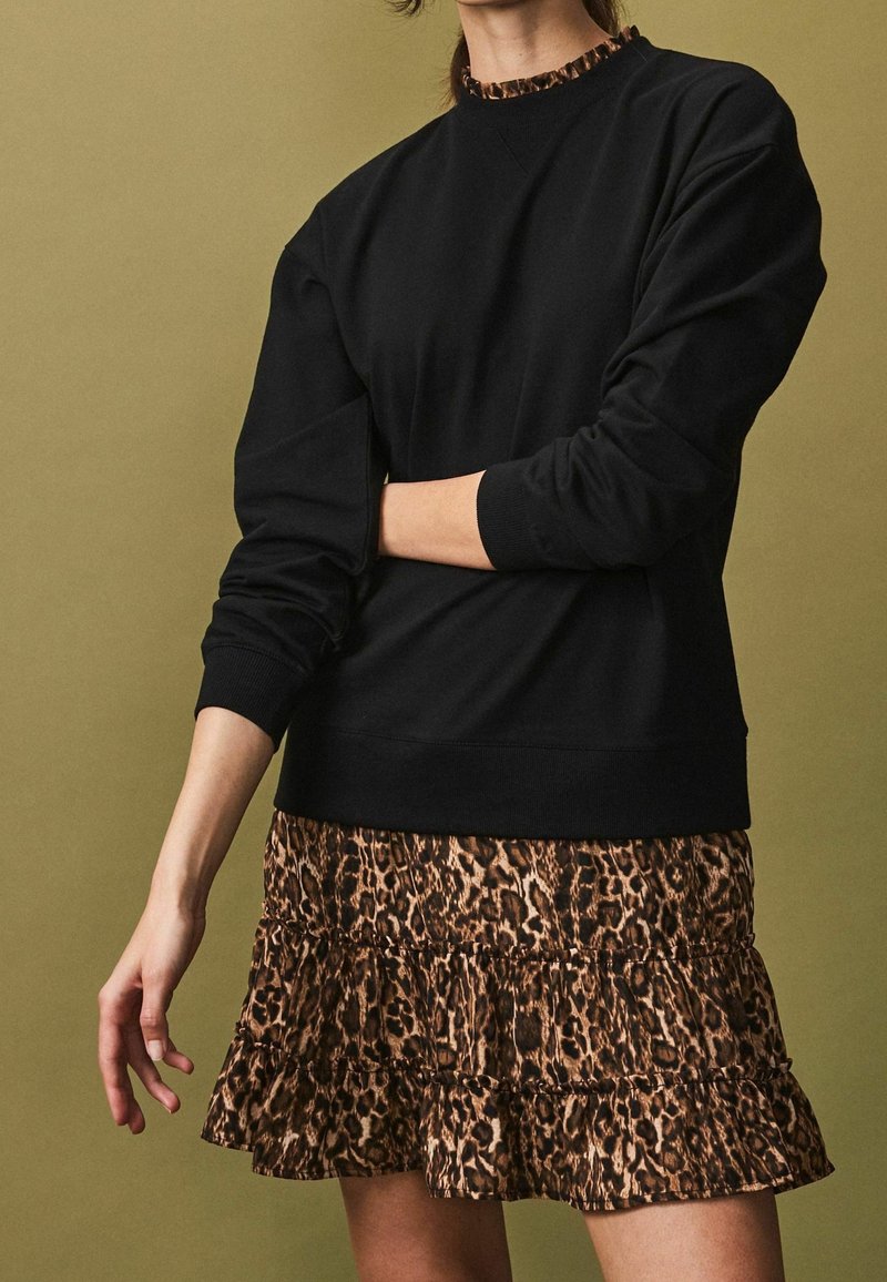 Sweat-shirt noir avec un col rond et des poignets côtelés, associé à une jupe à volants arborant un motif léopard marron.