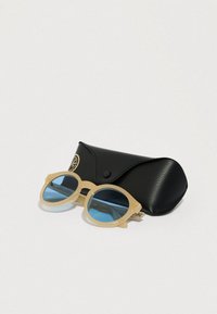 Világos bézs színű napszemüveg kerek kerettel és kék lencsékkel, egy fekete bőr tok mellett, arany logóval.