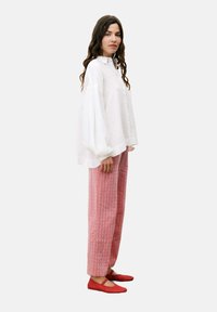 Witte oversized button-up shirt, roze gestreepte broek met wijde pijpen en rode ballerina's. Het shirt heeft een gestructureerde stof met een relaxte pasvorm.