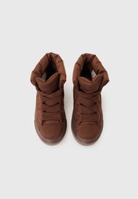 Zapatillas altas acolchadas de color marrón con cordones texturizados, punta redondeada y suave forro de piel sintética en el cuello. Suela de goma con detalles sutiles.
