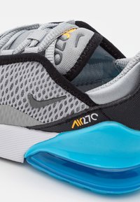 La zapatilla Nike Air Max 270 presenta una parte superior de malla gris, acentos negros y una unidad de amortiguación de aire azul. Detalles notables de logo y costura están presentes.