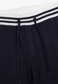 Marineblå sweatpants med en hvid ribbet talje, der har tre vandrette striber og sorte snore. Blødt materiale, elastisk pasform.