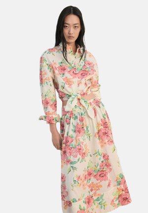 Vestido floral de tela ligera, con flores rosas y verdes sobre un fondo crema, cintura atada y mangas largas.