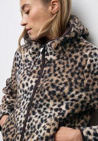 Fodraljacka i leopardmönster med hög krage, dragkedja och kontrasterande bruna detaljer. Mjuk textur och avslappnad passform.