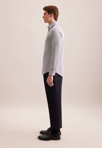 Camicia a scacchi azzurri chiari con colletto classico, abbinata a pantaloni navy scuri e scarpe di pelle nere. Semplici bottoni sui polsini.