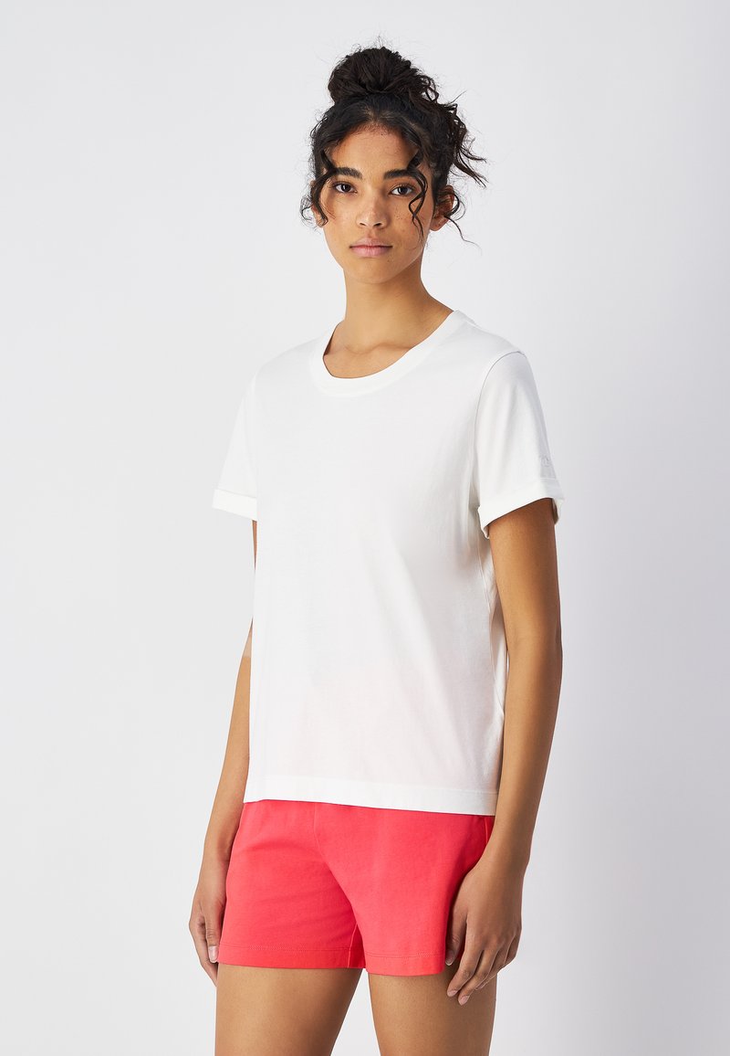 Witte katoenen T-shirt met korte opgerolde mouwen, wijde ronde halslijn en een ontspannen pasvorm, gecombineerd met fel koraalkleurige shorts.