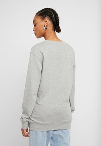 Sweatshirt cinza com decote redondo e mangas longas, apresentando uma textura têxtil suave. Combinado com jeans azul claro, mostrando um corte descontraído.