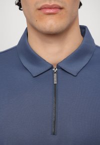 Mørkeblå polo-shirt med lynlås. Har en blød tekstur og et klassisk krave-design, der fremhæver en strømlinet silhuet.