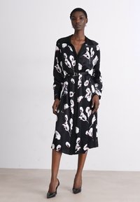 Černé šaty vyrobené z hedvábného materiálu, zdobené bílými květinovými vzory. Mají dlouhé rukávy, pásek v pase a střední délku.