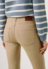 Bež klase skinny jeans s zadnjimi žepi, z usnjenim logotipom. Oblečen z modro-belim prugastim puloverjem, ki ima ribane manšete.