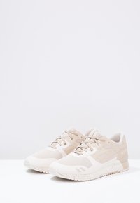 Béžové sportovní boty s textilním svrškem, šněrováním vpředu, polstrovaným límcem a texturovanou podrážkou. Obsahují jemné akcenty a moderní design.