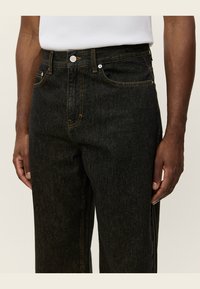 Vaqueros de denim negro con un corte recto, con costuras amarillas, bolsillos frontales, cierre de botón y una cintura de altura media.