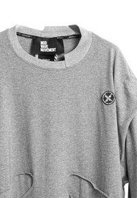 Sudadera gris fabricada con una mezcla de algodón, con detalles desgastados, cuello redondo y un parche circular negro en el pecho.