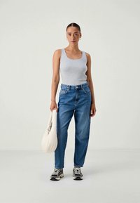 Sivý priliehavý top bez rukávov, svetlomodré džínsy s vysokým pásom, svetlo béžová kabelka a sivé tenisky s čiernymi akcentmi. Model stojí na svetlom pozadí.
