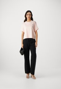 Rosa avkuttet t-skjorte med korte ermer og en liten logo på brystet, kombinert med høytidte svarte baggyjeans og beige høye sandaler.