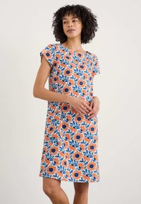 Ziedu kleita ar baltu pamatu, kas rotāta ar spilgti oranžām saulespuķēm un ziliem lapām, īsām piedurknēm un brīvi pieguļošu siluetu.