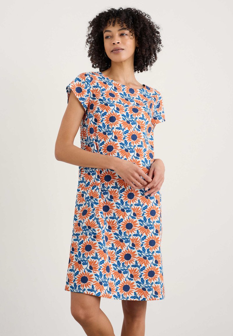 Ziedu kleita ar baltu pamatu, kas rotāta ar spilgti oranžām saulespuķēm un ziliem lapām, īsām piedurknēm un brīvi pieguļošu siluetu.