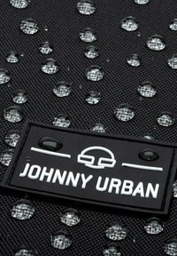 Černá texturovaná látka s kapkami vody, s výraznou obdélníkovou černou nášivkou, na které je v bílých písmenech napsáno "JOHNNY URBAN".