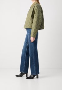 Quiltet olivengrøn jakke med krave, parret med højtaljede vide blå jeans og glansfulde sorte hæleboots.