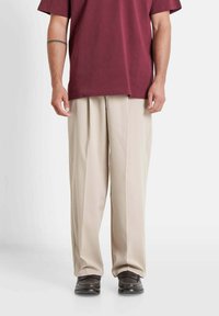 Burgundy short-sleeve shirt, beige pleated trousers, and black shoes. Trousers have a loose fit and fall to the ankles.