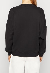 Svart oversized sweatshirt med sänkt axel, ribbade mudd, och fåll. Mjuk tyg med en slät yta. Enkelt mönster, inga synliga motiv.