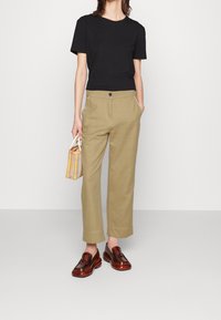 Black short-sleeve t-shirt, beige high-waisted trousers, brown glossy loafers, holding a small yellow plaid bag.