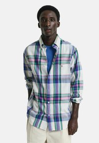 Camisa de cuadros multicolor con patrones en azul, verde, rosa y blanco, con botón en la parte delantera y mangas dobladas. Se lleva sobre una camiseta azul.