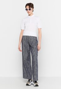 White polo shirt with short sleeves, paired with textured gray wide-leg pants. Model wears round sunglasses and sporty sneakers.