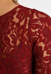 Burgundy blommig spets tyg med intrikata detaljer och öppen väv. Designen har lager av blommönster och ett slätt underlager.