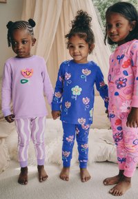 Kolme lasta kannavad värvilisi pidžaamasid: lilla ülaosaga, millel on lilleapplikaat, sinine lillemustriga ja roosa lillemustritega.