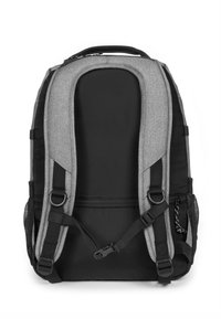 Mochila de tela gris con acentos negros. Cuenta con correas acolchadas, un asa superior y bolsillos laterales de malla. Diseño elegante y estructurado.