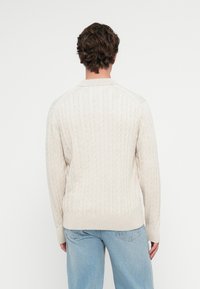 Kabelstrickpullover in hellem Creme mit gerippten Bündchen und Saum. Verfügt über einen klassischen Kragen und lange Ärmel, hergestellt aus einem weichen, strukturierten Stoff.