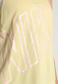 Top sin mangas amarillo con grandes letras en mármol rosa. La tela es suave con un ligero brillo y un corte relajado. Sin patrones adicionales.