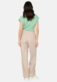 Svetlo zelena kratka majica, bež hlače visoko pasu in bele superge s pastelnimi akcenti. Tekstura se zdi gladka in sproščena.