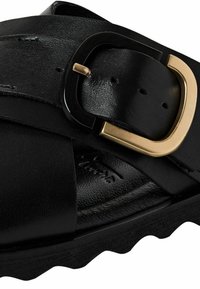 Black leather sandal featuring a wide strap and a prominent gold and black buckle. Textured footbed and rubber sole with a zigzag pattern.