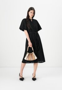Abito nero con occhielli, maniche corte e larghe e una cintura. Abbinato a una borsa multicolore con manico intrecciato e scarpe con tacco a punta.