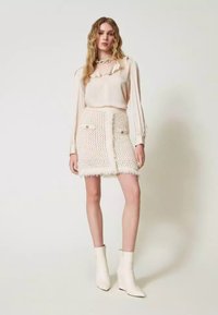 Blusa crema con scollo arricciato e maniche lunghe abbinata a una gonna crema testurizzata con due tasche e orlo sfilacciato. Stivaletti con zeppa.