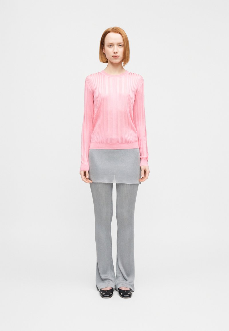 Ροζ μακρυμάνικη μπλούζα με ριμπ ύφανση, συνδυασμένη με γκρι φούστα με στρώσεις και εφαρμοστά γκρι παντελόνια με καμπάνες. Τα παπούτσια είναι μαύρα με στρογγυλεμένες μύτες.