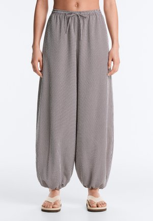Femme portant un pantalon ample à carreaux avec des ourlets élastiques et une taille à cordon, associé à des sandales à plateforme beige.